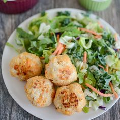 a white plate topped with meatballs next to a salad and cupcakes on a table