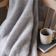 a cup of coffee sits on top of a book, next to a gray blanket