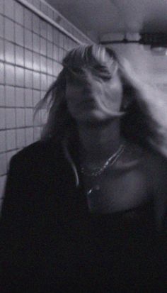 a woman standing in a bathroom next to a wall with tiles on it and her hair blowing in the wind