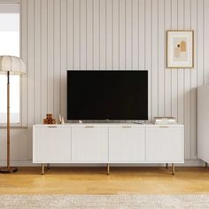 a flat screen tv sitting on top of a white cabinet in a living room next to a lamp