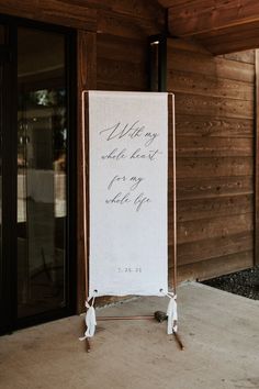 a white sign with writing on it sitting in front of a wooden wall and door