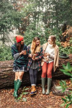 three young women sitting on a log in the woods looking at their cell phones and laughing