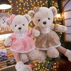 two teddy bears dressed in pink and brown are hanging from a string with lights behind them