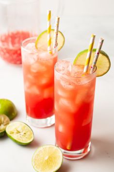 two glasses filled with drinks next to limes