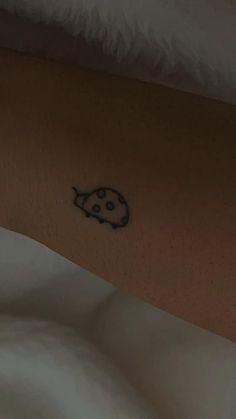 a ladybug tattoo on the arm of a person with white sheets and pillows