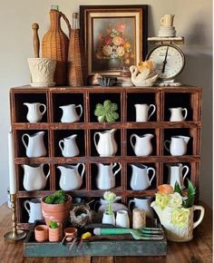 a wooden shelf filled with white vases and other items on top of a table