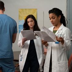 two women in white lab coats are looking at papers while another woman stands behind them