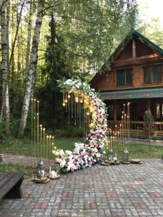 a wedding arch is decorated with flowers and candles in front of a log cabin on a brick patio