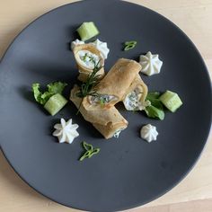 a black plate topped with food and veggies on top of a wooden table