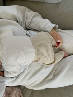 a woman laying on top of a couch covered in blankets and holding a stuffed animal