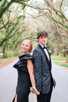 a young man and woman dressed in formal wear posing for a photo on the road