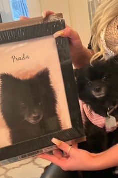 a woman holding two small dogs in her arms and one is holding a framed photo