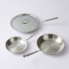 three stainless steel pots and pans on a white surface with the lid open, one empty