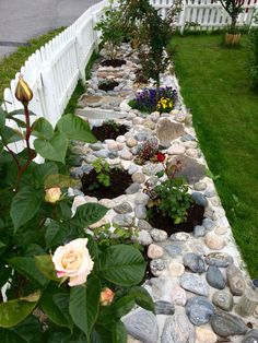 a white picket fence with flowers and rocks in the garden next to it on grass