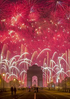 fireworks are lit up in the sky above an arch and street with people walking on it