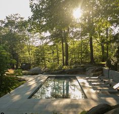 an outdoor pool surrounded by trees and rocks with sun shining through the trees behind it