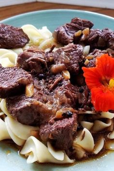 a blue plate topped with pasta and meat next to a red flower on top of it