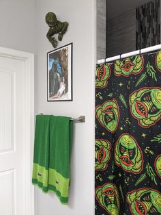 a green towel hanging on the wall next to a white door with an alien themed shower curtain