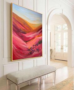 a large painting hanging on the wall above a bench in a room with white walls