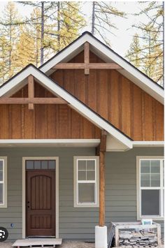 a gray house with wood trim and white trim on the front door is shown in this image