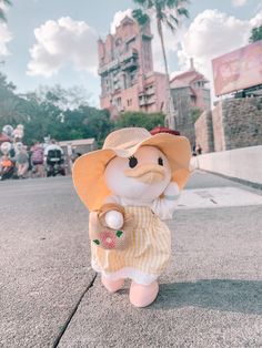 a small stuffed animal wearing a yellow dress and sun hat standing on the side walk