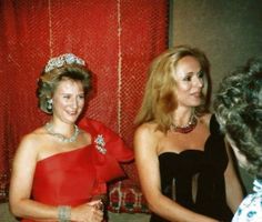 two women dressed in evening wear talking to each other and smiling at one another while wearing tiaras