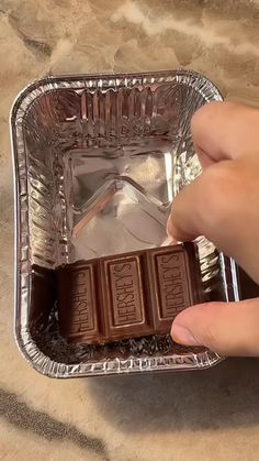 someone is holding three pieces of chocolate in a foil container with ice cubes on top