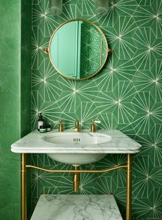 a white sink sitting under a bathroom mirror next to a green wall with geometric designs on it