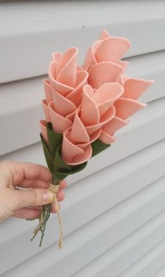 a hand holding a bunch of pink flowers on top of a window sill next to a white building