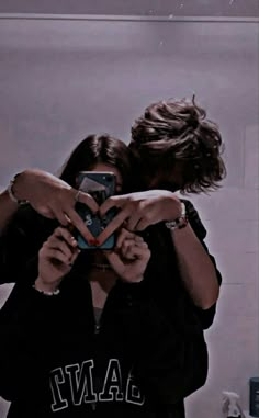 two people standing in front of a mirror taking a selfie with their cell phone