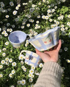 someone is holding their coffee cup in front of some daisies