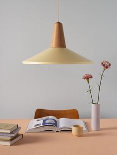 an open book on a table next to a vase with flowers in it and a lamp hanging from the ceiling