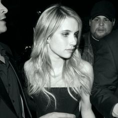 a black and white photo of a woman in a dress talking to two men at a party