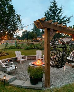 an outdoor fire pit with chairs around it and string lights strung across the top area