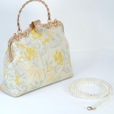 a white purse with yellow flowers on it next to a pearl necklace and chain bracelet