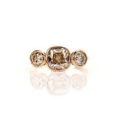 three stone ring in yellow gold with white and brown diamonds on the sides, set against a plain background