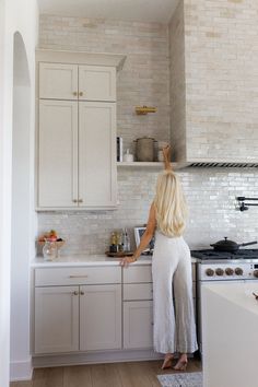 a woman is standing in the kitchen with her hand on the stove top and looking at the sink