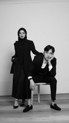 two people sitting on a chair in front of a wall and one is wearing a black coat