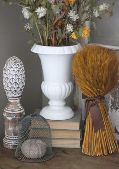 a white vase filled with lots of flowers next to books and knick knacks