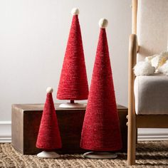 three red knitted christmas trees sitting on top of a wooden table