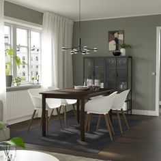 a dining room table with white chairs in front of a gray wall and wooden floor