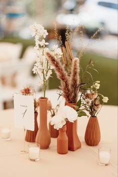 three vases with flowers are sitting on a table next to some candles and cards