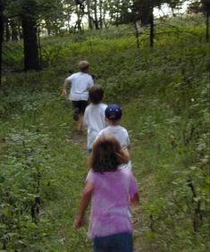 three children are running down a path in the woods