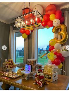 a table with balloons and other items on it in front of a window that is open