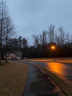 an empty street at night with the lights on and trees in the background, along with some houses