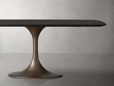 an oval dining table with a black top and gold base, in front of a gray wall