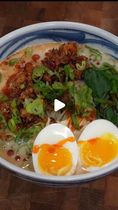 a bowl filled with eggs, meat and greens on top of a wooden table next to a