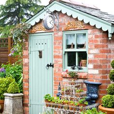 a small brick building with potted plants and a clock on the window sill