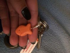 a person holding a keychain with a small orange fish on it's side