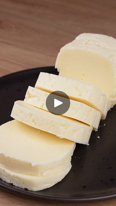 a black plate topped with sliced cheese on top of a wooden table